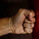 A detailed close-up of a clenched fist striking a red surface showcasing strength.