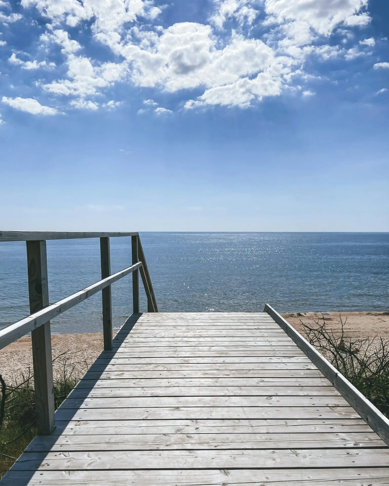 Beautiful boardwalk leading to a serene ocean view under a blue sky with fluffy clouds.