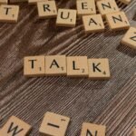 Wooden letter tiles on a table spelling 'Talk', ideal for language and communication themes.