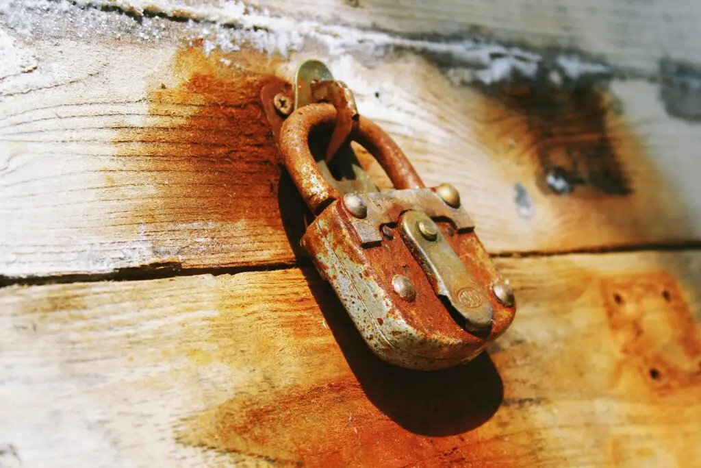 Close-up of a rustic, rusted padlock hanging on a weathered wooden door, symbolizing protection and security.