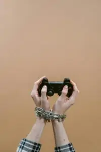Hands chained playing video game with controller illustrating digital addiction concept.