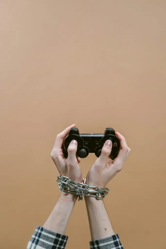 Hands chained playing video game with controller illustrating digital addiction concept.