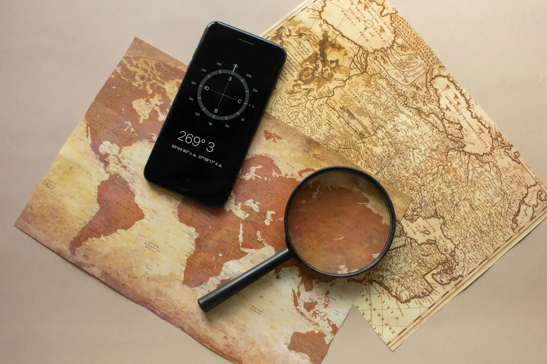 חיים של מטרה ושליחות Top view of magnifying glass and cellphone with compass with coordinates placed on paper maps on beige background in light room
